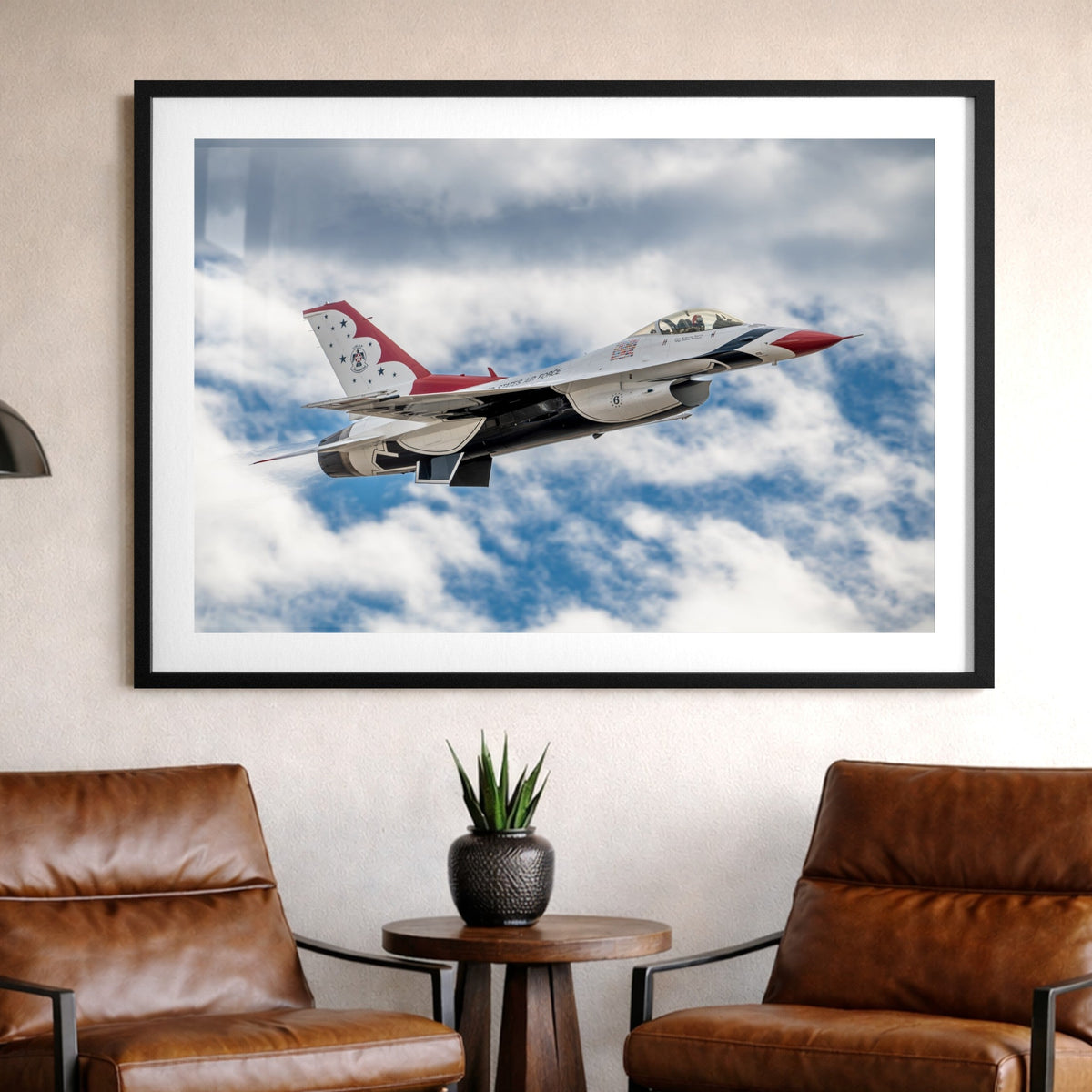 Framed photograph of a fighter jet against a blue sky with clouds in a living room setting.